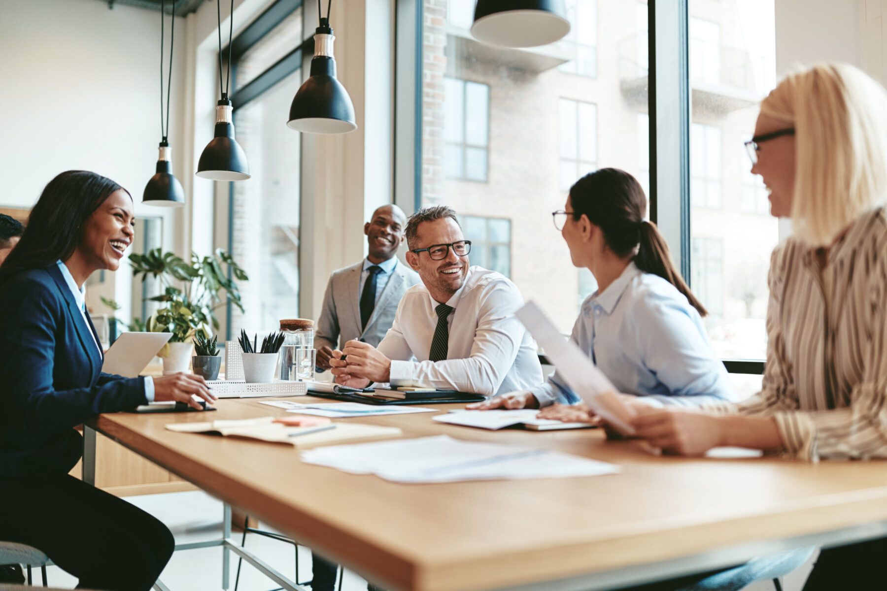 Professional business colleagues meet and laugh while seated at conference table in modern office