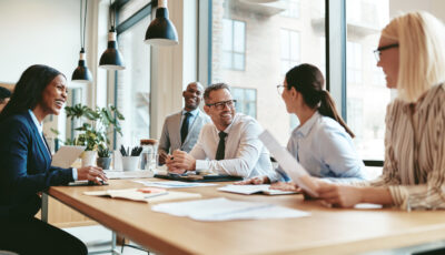 Professional business colleagues meet and laugh while seated at conference table in modern office